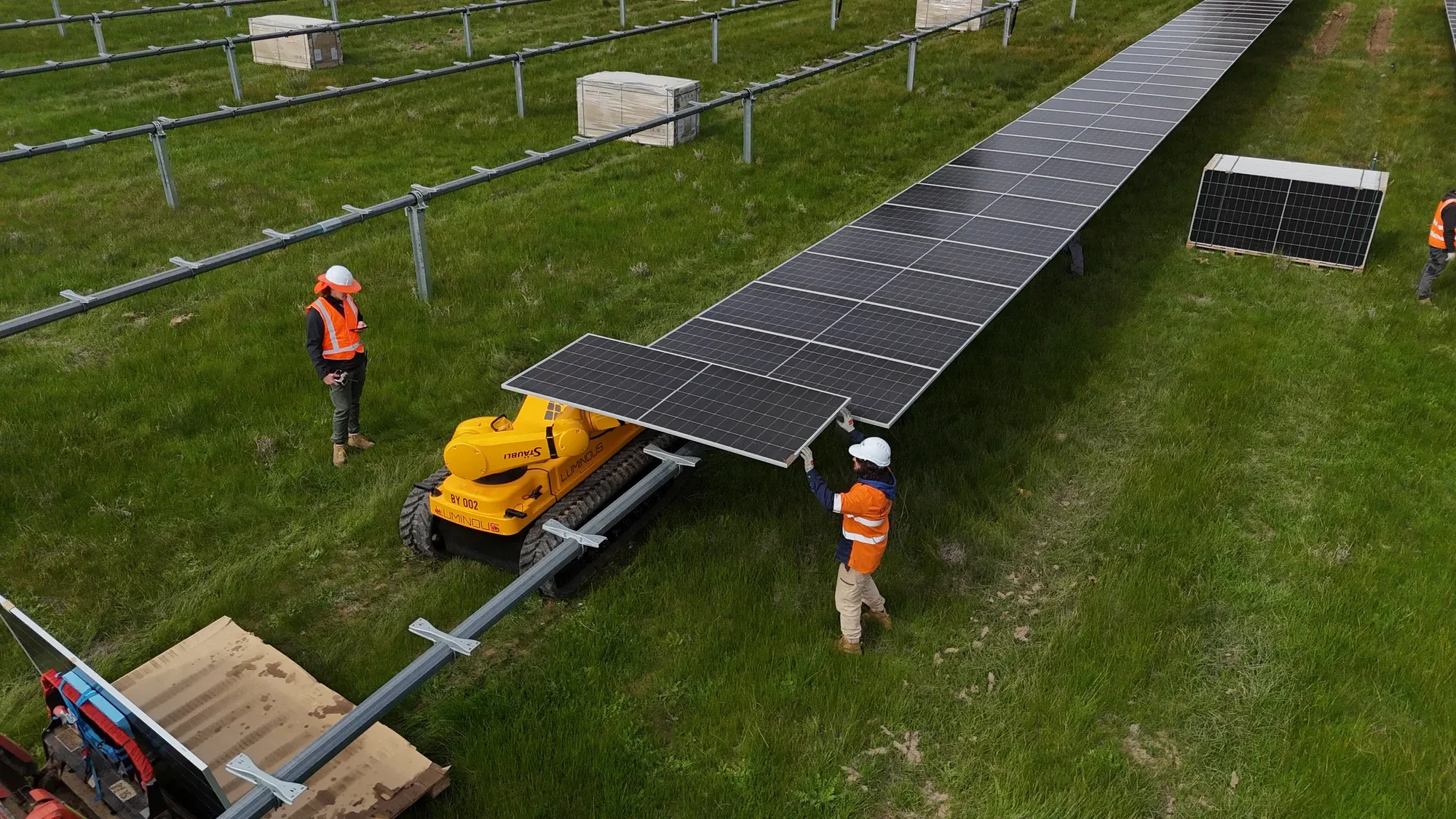 Drone view of a LUMI setting a solar module on a tracker at Goorambat East, a crew member on each side