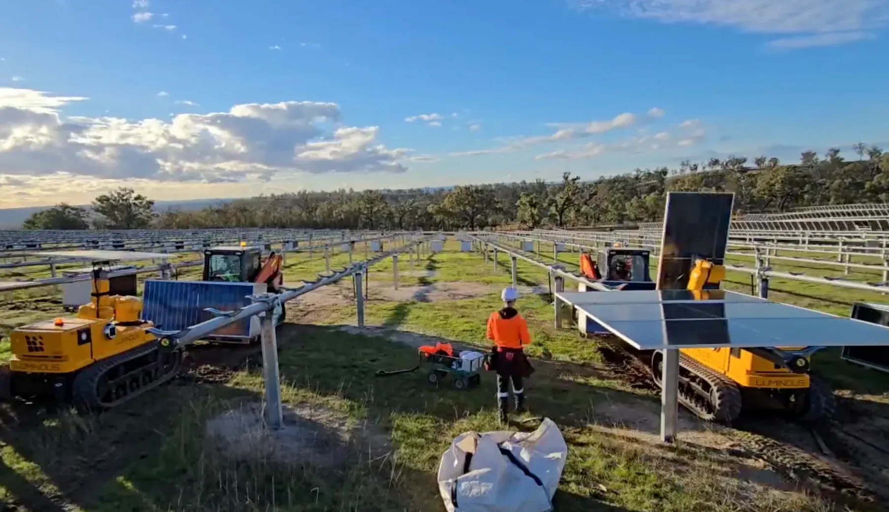 Two LUMIs setting solar modules on tracker rows at Goulburn River Solar Farm, a crew member between them
