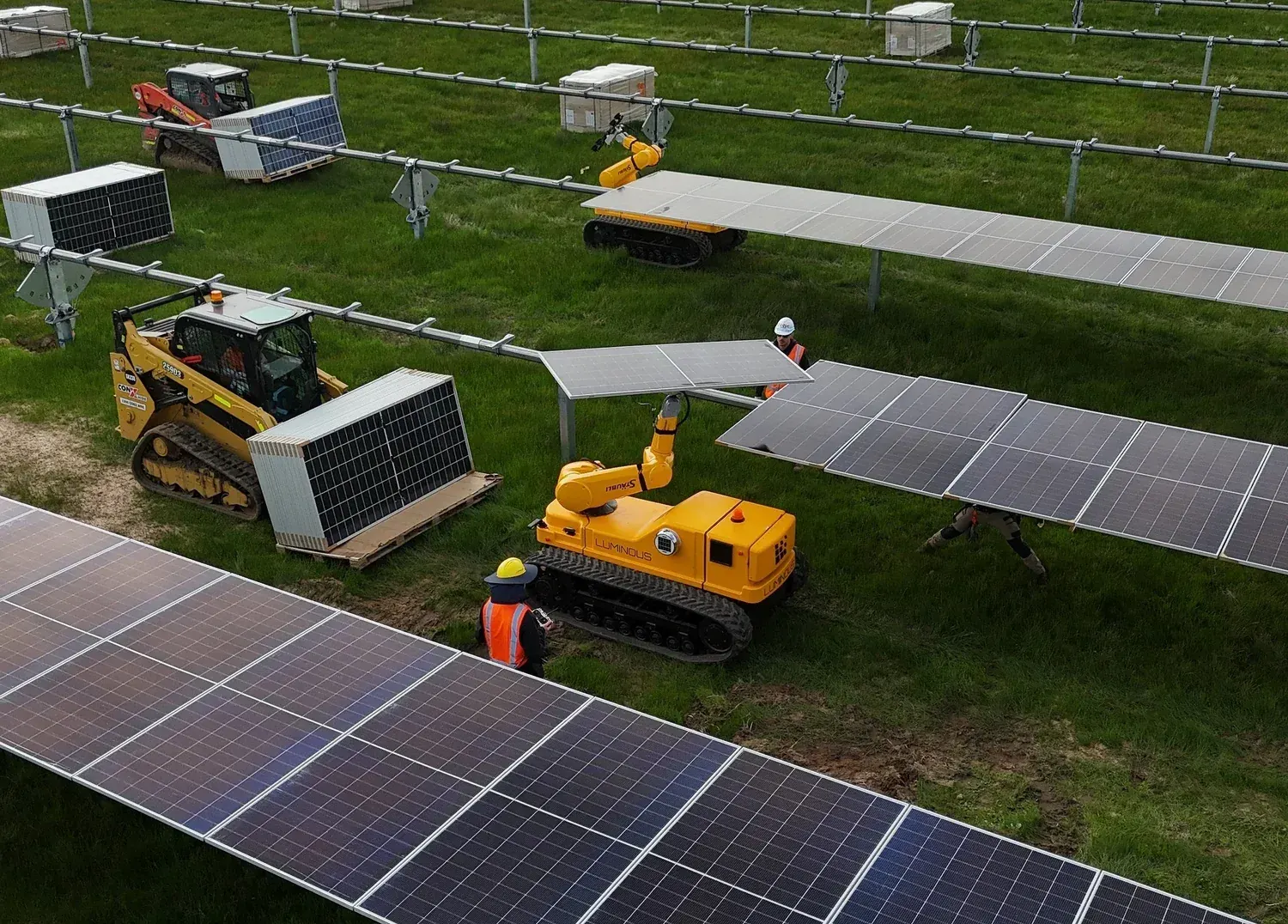 A LUMI beside a pallet of solar modules, lifting a module toward the tracker