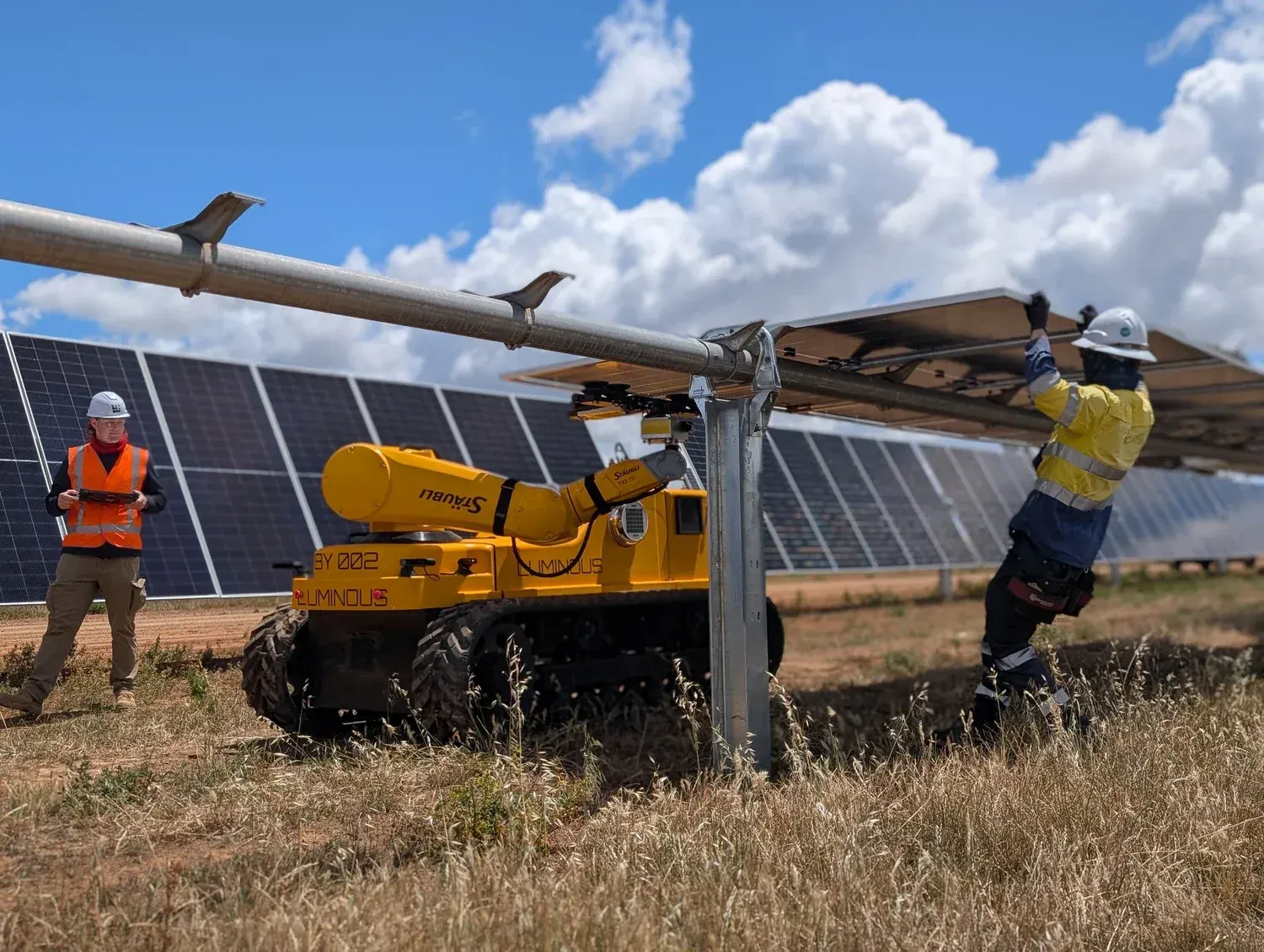 An operator with a tablet watches a LUMI place a solar module while a crew member guides it